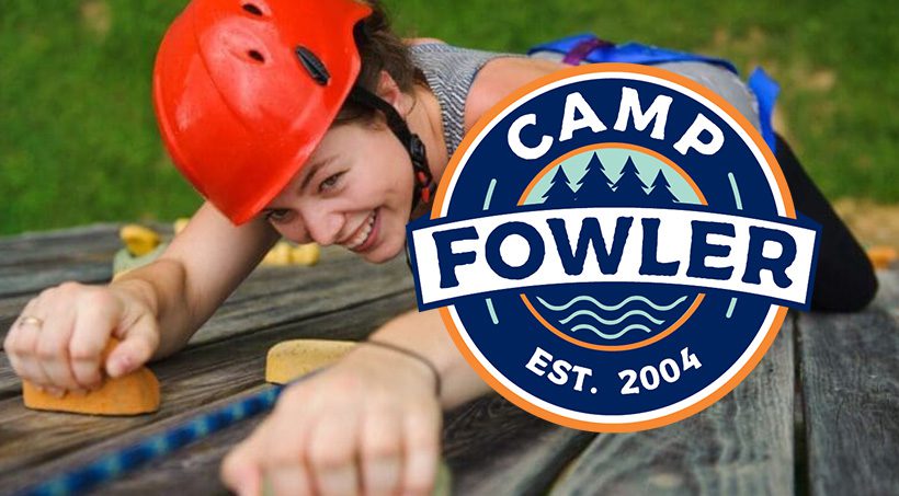Camper rock climbing at Camp Fowler wearing a red helmet and harness