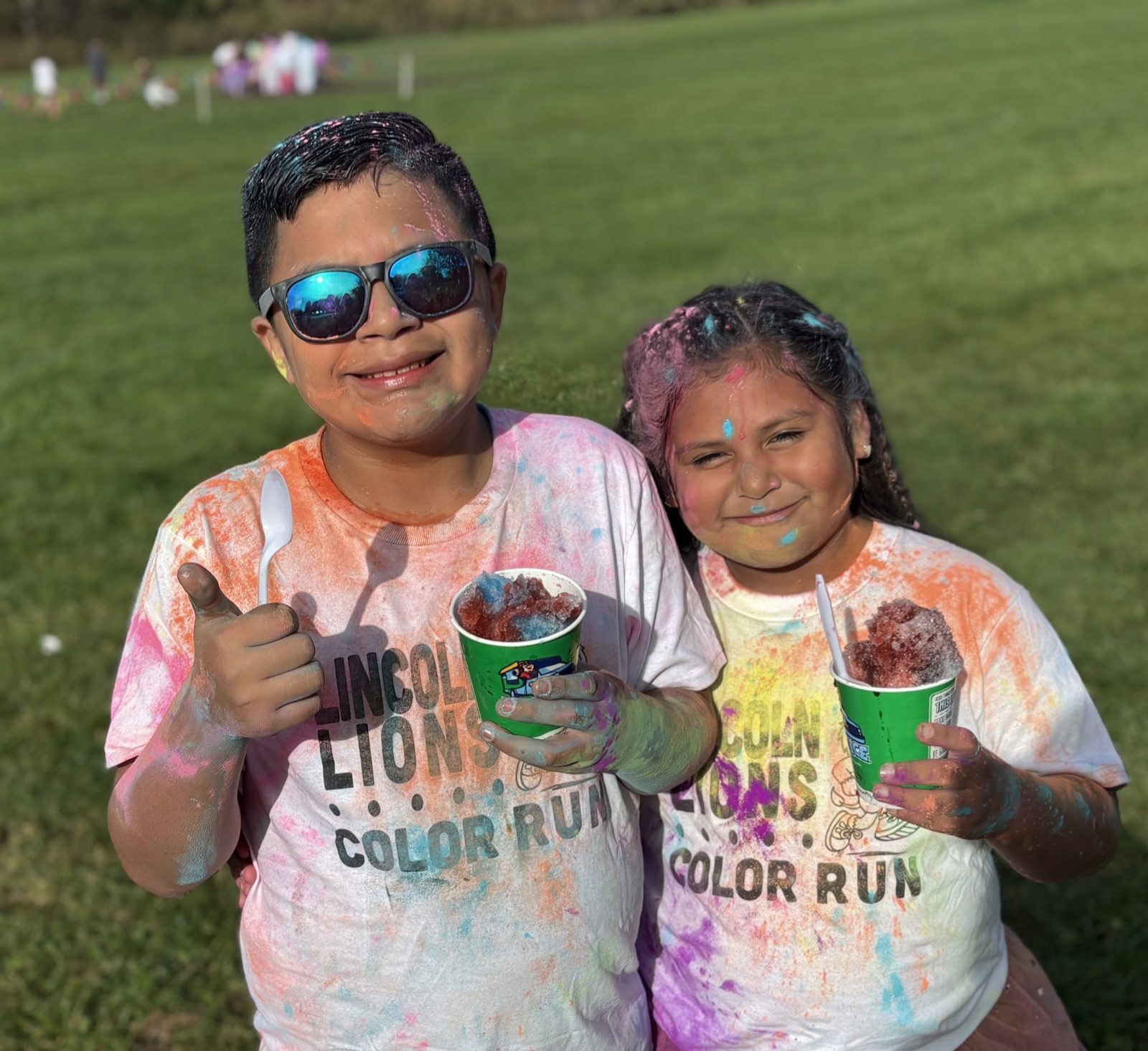 Two Lincoln Elementary students covered in colored powder smile with snow cones after the Lincoln Lions Color Run