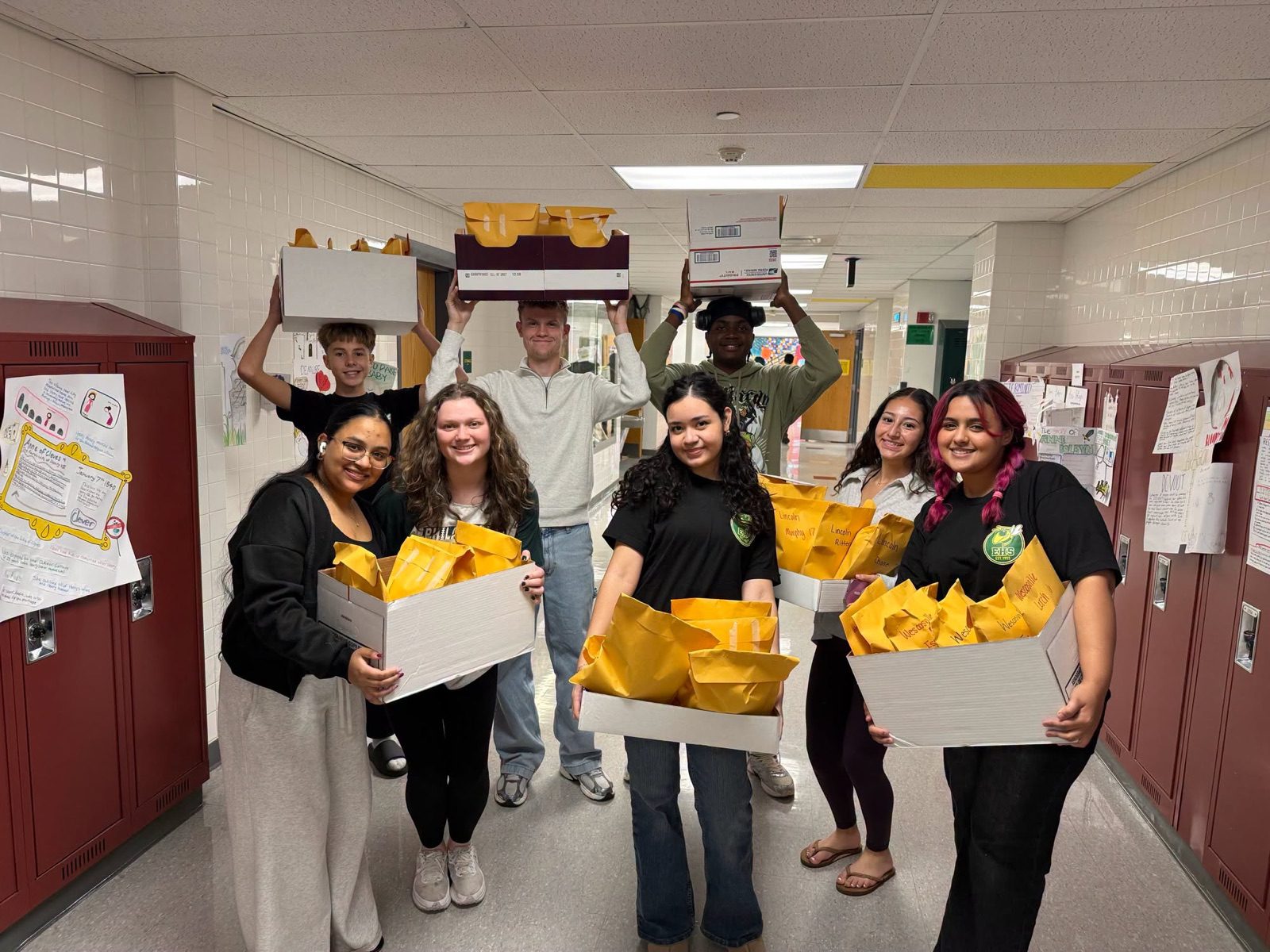 Emmaus High School students in a hallway hold up boxes of yellow gift bags