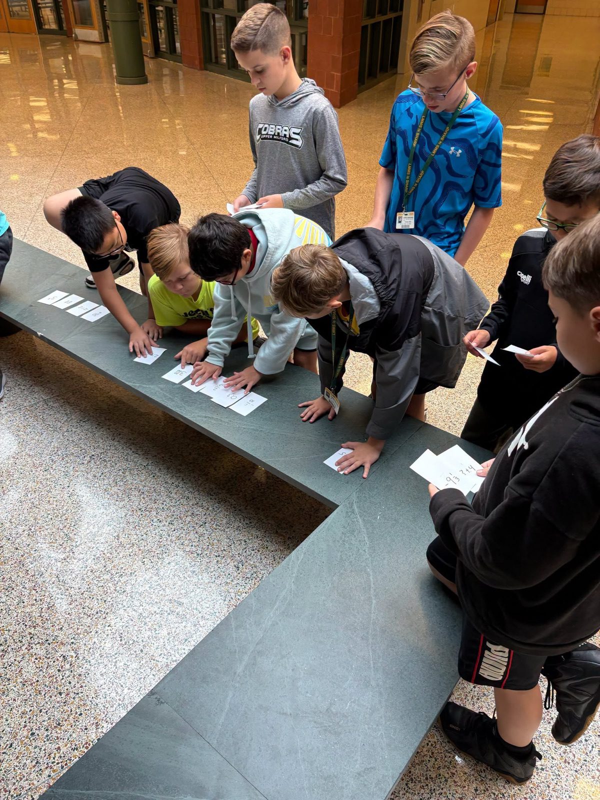 Middle school students lean over a bench to sort cards together during a group activity